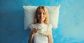 Lazy woman waking up after sleeping on white soft comfortable pillow imagining she lying on the bed holds cup of coffee on blue