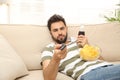 Lazy young man with chips and drink watching TV on sofa Royalty Free Stock Photo