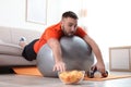 Lazy young man on exercise ball reaching for chips