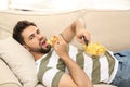 Lazy young man with potato chips watching TV on sofa at home Royalty Free Stock Photo