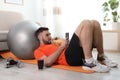 Lazy young man with smartphone eating junk food on yoga mat