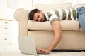 Lazy young man using laptop while lying on sofa at home