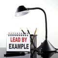 LEAD BY EXAMPLE text on notebook with pen and table lamp on the black background Royalty Free Stock Photo