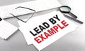 LEAD BY EXAMPLE text on a paper with keyboard, calculator on grey background Royalty Free Stock Photo