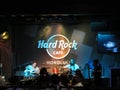 Lead singer of Guidance Band sings into mic while wearing sunglasses as he Jams on guitar on stage at Hard Rock Cafe