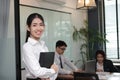 Leadership business woman concept. Cheerful young Asian businesswoman with ring binder standing against her colleague in office ba Royalty Free Stock Photo