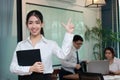 Leadership business woman concept. Cheerful young Asian businesswoman with ring binder standing against her colleague in office ba Royalty Free Stock Photo