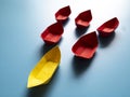 Leadership Concept - Yellow color paper ship origami leading the rest of the red paper ship on blue cover background Royalty Free Stock Photo