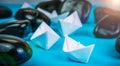 Leadership white paper boat lead further ships between abstract rock stones on blue background. Light flares right top Royalty Free Stock Photo