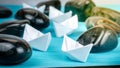 Leadership white paper boat lead further ships between abstract rock stones on blue background. Light flares right top Royalty Free Stock Photo