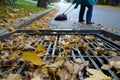 leafcovered storm drain with person sweeping nearby