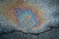 Leakage of oil or gasoline from a car onto a wet, cracked asphalt road.