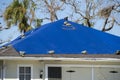 Leaking house roof covered with protective tarp sheets against rain water leaks until replacement of asphalt shingles
