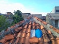 The leaky tyle roof of the house has been patched. Background some houses and evening sky.