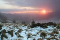 From the lean covered by snow there is a view opened to the mountains, morning fog and sunset. Sun rays lighten up the sky.