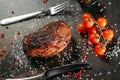 A lean piece of seared steak on the table, next to which are cutlery fork and knife, as well as a sprig of cherry tomatoes, a