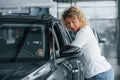 Leaning on the car. Woman with curly blonde hair is in autosalon