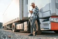 Leaning by the vehicle and using phone. Young truck driver is at daytime Royalty Free Stock Photo