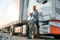 Leaning by the vehicle and using phone. Young truck driver is at daytime Royalty Free Stock Photo