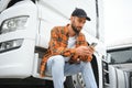 Leaning by the vehicle and using phone. Young truck driver is at daytime Royalty Free Stock Photo