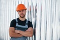 Leaning on the wall. Serious industrial worker indoors in factory. Young technician with orange hard hat Royalty Free Stock Photo