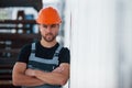 Leaning on the wall. Serious industrial worker indoors in factory. Young technician with orange hard hat Royalty Free Stock Photo