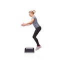 Leaping up in pursuit of fitness. A smiling young woman doing aerobics on an aerobic step against a white background.
