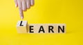 Learn or earn symbol. Businessman hand points at turned wooden cubes with words Earn and Learn. Beautiful yellow background. Royalty Free Stock Photo