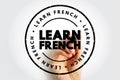 LEARN FRENCH circular stamp emblem with bold text layered over a hand holding a marker, symbolizing language learning, education, Royalty Free Stock Photo
