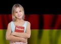 Learn German language concept. Beautiful young girl holding book with inscription German in German language on flag of Germany Royalty Free Stock Photo