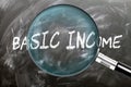 Learn, study and inspect Basic Income. A magnifying glass enlarging word \'basic income\' written on a blackboar Royalty Free Stock Photo