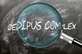Learn, study and inspect Oedipus Complex. A magnifying glass enlarging word \'oedipus complex\' written on a bla Royalty Free Stock Photo
