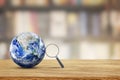 Magnifying glass lean on blue planet earth with blurry image of library room in background.