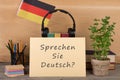 paper with text & x22;sprechen sie deutsch?& x22;, flag of the Germany, books, headphones, pencils