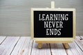 Learning Never Ends text written on chalkboard with easel on wooden background Royalty Free Stock Photo