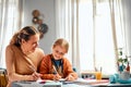 Learning new together. Easygoing lady looking at kid sitting at corner of desktop and doing exercises