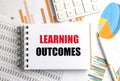Learning outcomes message on notepad with charts, spreadsheets, pen and calculator on desk Royalty Free Stock Photo