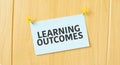 LEARNING OUTCOMES sign written on sticky note pinned on wooden wall Royalty Free Stock Photo