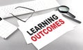 Learning outcomes text on a paper on a gray background near a calculator and a white keyboard Royalty Free Stock Photo