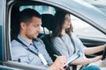 Learning to drive a car. Male instructor and female student practicing in driving. Young man notice results of test in