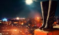 Leather boots standing on roof overlooking city at night