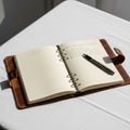 A leather bound notebook with a snap closure lies open on a white table Royalty Free Stock Photo