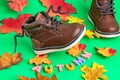Leather, brown, children\'s boots with laces and autumn leaves on green background. The word AUTUMN from bright letters.