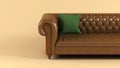 Leather brown sofa on wooden legs with quilted back and green fabric pillow on beige background front view. Stylish sofa, piece of Royalty Free Stock Photo