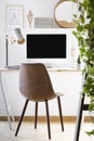 Leather chair standing by wooden desk with mockup monitor, metal lamp and decor in real photo of home office corner in white room