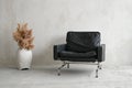 A leather chair and a vase with pampas grass in a room with a concrete wall, copy space. Minimalist composition interior
