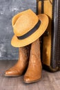 Leather cowgirl boots with a straw hat pattern and an old suitcase stand on the floor against a gray wall Royalty Free Stock Photo