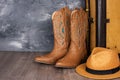 Leather cowgirl boots with straw hat pattern and an old suitcase stand on the floor against gray wall