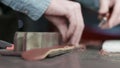 A leather craftsman is cutting the edges of a belt. The master is using an edge beveler tool.