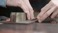 A leather craftsman is cutting the edges of a belt. The master is using an edge beveler tool.